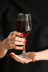 Hands with beautiful manicure holding glass of wine on dark background