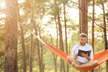 Young man with book relaxing in hammock outdoors