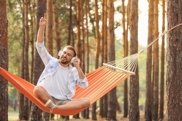 Young man listening to music while relaxing in hammock outdoors