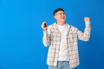 Happy Asian man with car key on color background