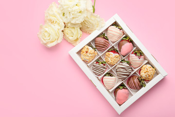 Box with tasty glazed strawberry and flowers on color background