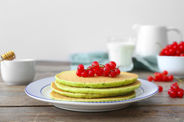 Plate with tasty green pancakes and berries on wooden table