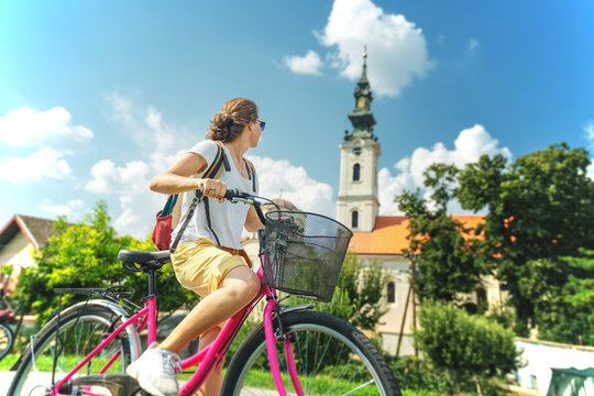 Young beautiful stylish girl travels by bicycle in Serbia. Stands against the background of an ancient temple