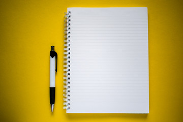 Flat lay of white and black pen and notepad on yellow background