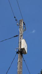 junction box with a counter with electric wires running in different directions on a wooden post against a blue sky background