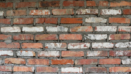 uneven brick wall of an old building interspersed with white long-painted areas among shades of red