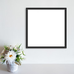 Black frame mockup on white wall with pot of flowers on white surface. Copy space.