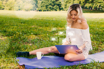 Pretty brunette woman lying in the grass and using laptop outdoor.