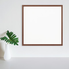 Wood frame mockup on white wall with philodendron leaf in vase on white surface. Dark wood. Copy space.