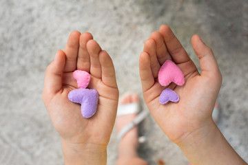 The child's hand holds violet nad rose handmade hearts in the palms. Concept of foster parents,...