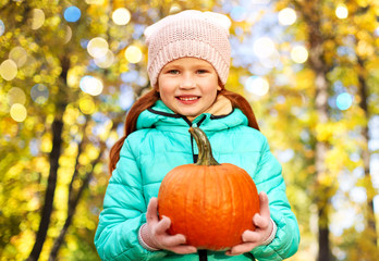 Fototapeta premium childhood, season and people concept - happy redhead girl with pumpkin at autumn park over festive lights