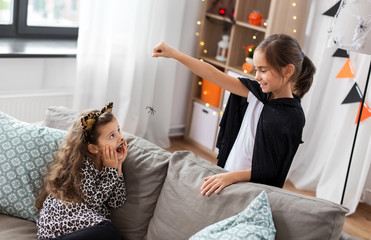 halloween, holiday and childhood concept - smiling little girls in party costumes playing with toy spider at home
