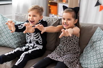 halloween, holiday and childhood concept - smiling little boy and girl in party costumes having fun at home