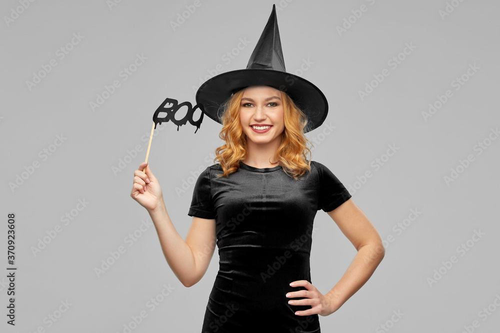 Sticker holiday and photo booth concept - happy smiling woman in black halloween costume of witch with party accessory over grey background