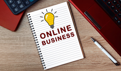 Notebook with text ONLINE BUSINESS. Notebook on desk with laptop and a pen.