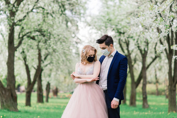 Young loving couple walking in medical masks in the park during quarantine on their wedding day. Coronavirus, disease, protection, sick, illness flu europe celebration canceled.
