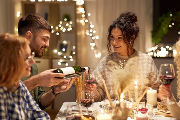 holidays and celebration concept - happy friends having christmas dinner at home pouring non-alcoholic red wine