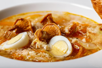 Close-up soup with chanterelles and vegetables with fried croutons. Delicious recipe with wild mushrooms, organic vegetables and quail eggs.