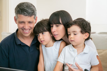 Happy parent and two kids looking at computer display, sitting on couch together. Medium shot. Communication or entertainment internet concept