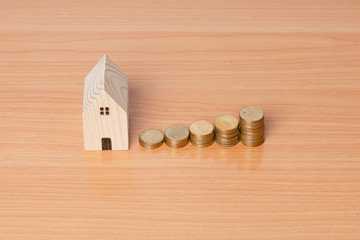 Money coin saving with a wooden home model on a wooden background.