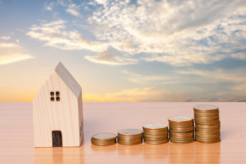 Money coin saving with a wooden home model on evening sky background.