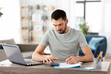 remote job and business concept - man with papers, calculator and laptop computer working at home office