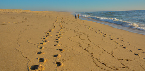 footprints on the beach sand back and forth, with two people walking back.