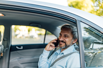 Man with grey hair and grey beard in a car,using phone.