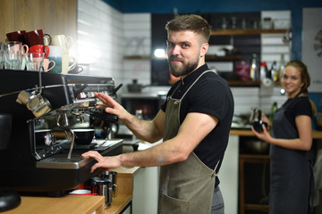 A young barista guy makes coffee on a large professional coffee machine. Small business and work concept for young people