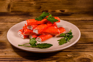 Ceramic plate with pile of crab sticks and parsley twig on a wooden table
