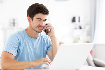 Friendly man talking phone and work at home with laptop computer, freelance.