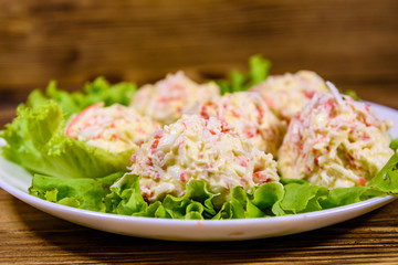 White plate with crab-cheese balls and lettuce leaves on wooden table