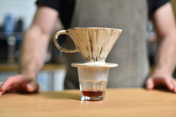 A young barista guy is making coffee with boiling water and a filter. Brewed coffee