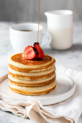 Maple syrup pouring pancakes with strawberry  and coffee cup on the table. Classic American breakfast concept