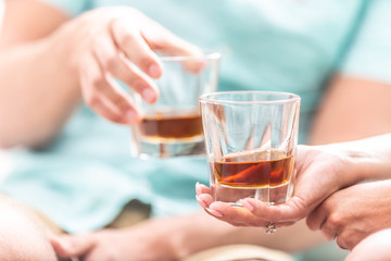 Man and woman hands toasting with glasses of whiskey brandy or rum indoors - closeup