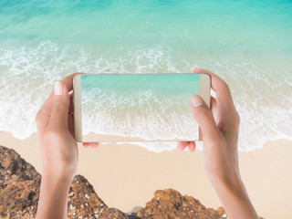 Hand woman Taking sea photo with mobileHand woman holding mobile with sand beach view on blur image of sand beach with white sea soft wave on top view .