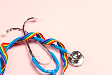 Stethoscope with LGBT rainbow ribbon on pink background.