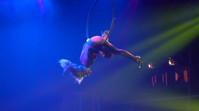 Flexible sexy athletic woman do spin on aerial hoop, aerial acrobatic hoop performance, women hold on aerial hoop with high heels backlit in yellow light, air circus show