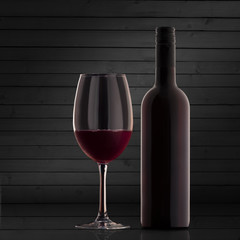 A bottle of red wine is standing next to a glass of wine on the background of wooden boards. Homemade wine showcase concept.