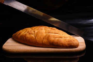 Homemade white bread is cut with a large knife. Baking at home.