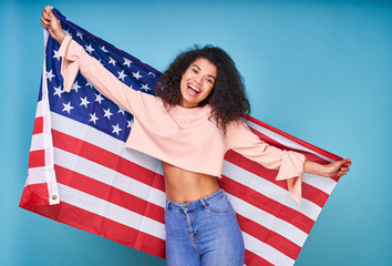 Smiling casual African woman holding USA flag isolated on blue background.