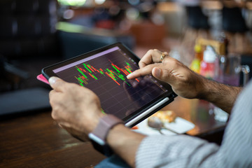 Asian business men using a tablet for working and checking stock trends chart and financial analysis at coffee shop