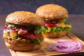 Two hamburgers served on  wooden cutting board board with purple onion slices. 