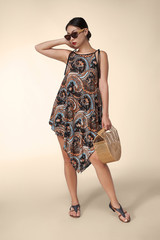 A young Asian lady in sunglasses is wearing leather sandals and loose summer dress with colorful...