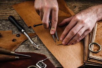 Close up of a shoemaker or artisan worker hands. Leather craft tools on old wood table. Leather craft workshop.