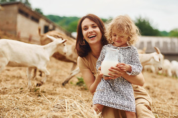 Fresh natural milk. Young mother with her daughter is on the farm at summertime with goats