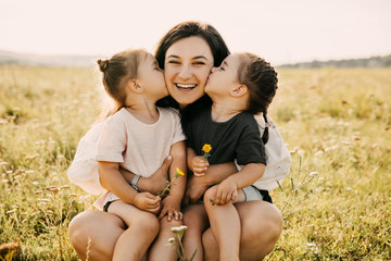 Mother and two daughters playing outdoors in a field. Girls kissing mother on cheeks.