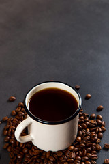 Black delicious coffee in an iron mug and scattered grains on a stone table. Authentic drink, copy space.