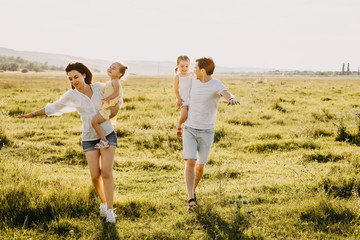 Family of four playing in a field on a summer day. Mother, father and two daughters running on green grass.