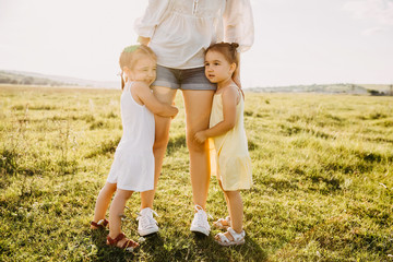 Fototapeta premium Mother and two daughters outdoors in an open field with green grass. Girls hugging mother.